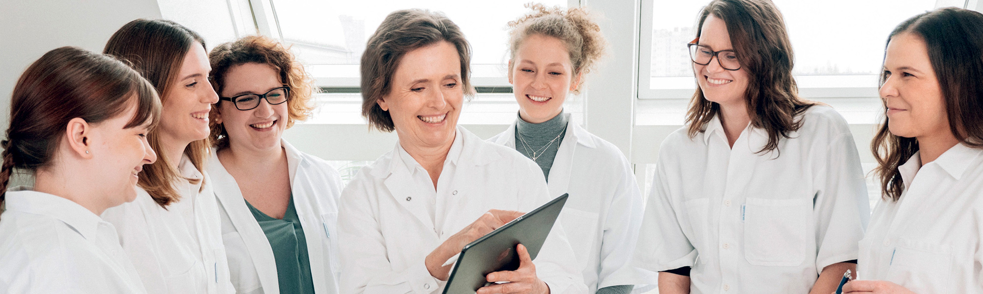 Gruppenfoto mehrerer Ärzte in weißen Kitteln, mit einer Frau die auf ein Tablet zeigt in der Mitte.