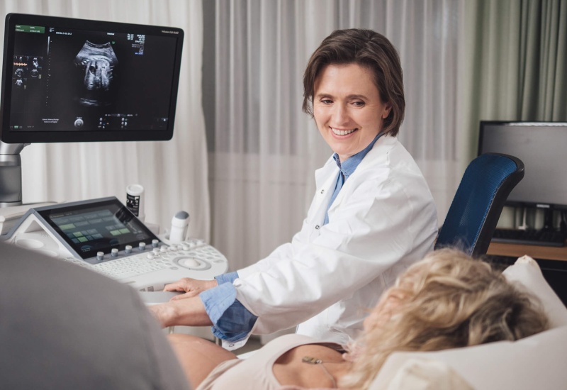 Ärztin in mitten einer Ultraschall-Untersuchung. Auf einem Bildschirm sieht man was der Ultraschall gerade erfasst.